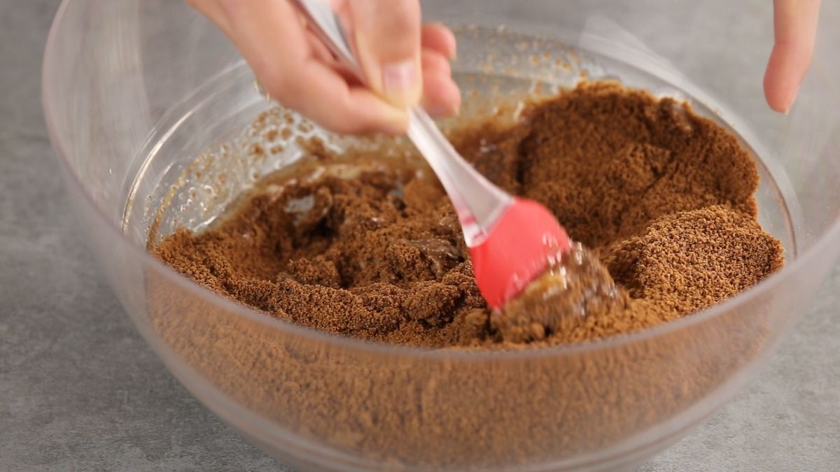 cookie crumbs and butter being mixed with pink spatula in glass bowl