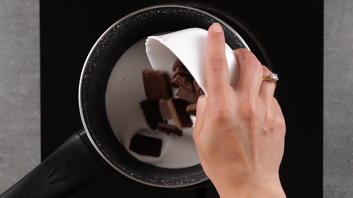 hand pouring chocolate into saucepan of heavy cream