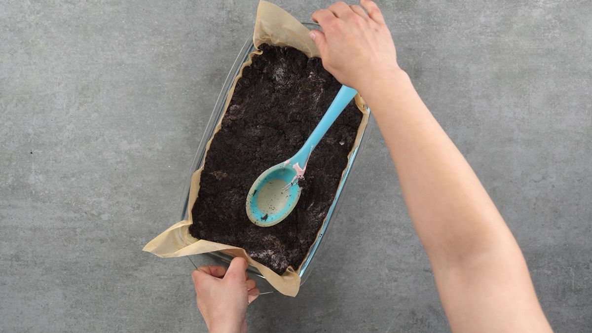 blue spoon spreading cookies and cream mixture into baking dish