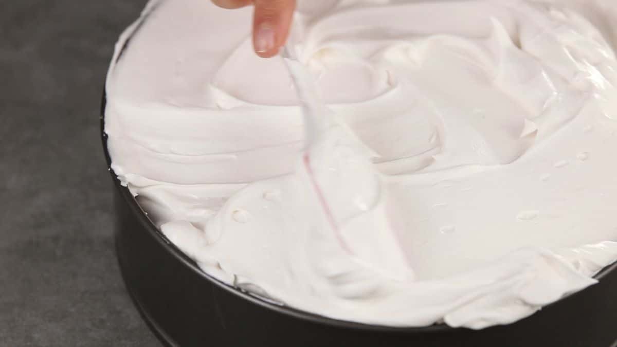 hand spreading whipped cream over the top of cheesecake