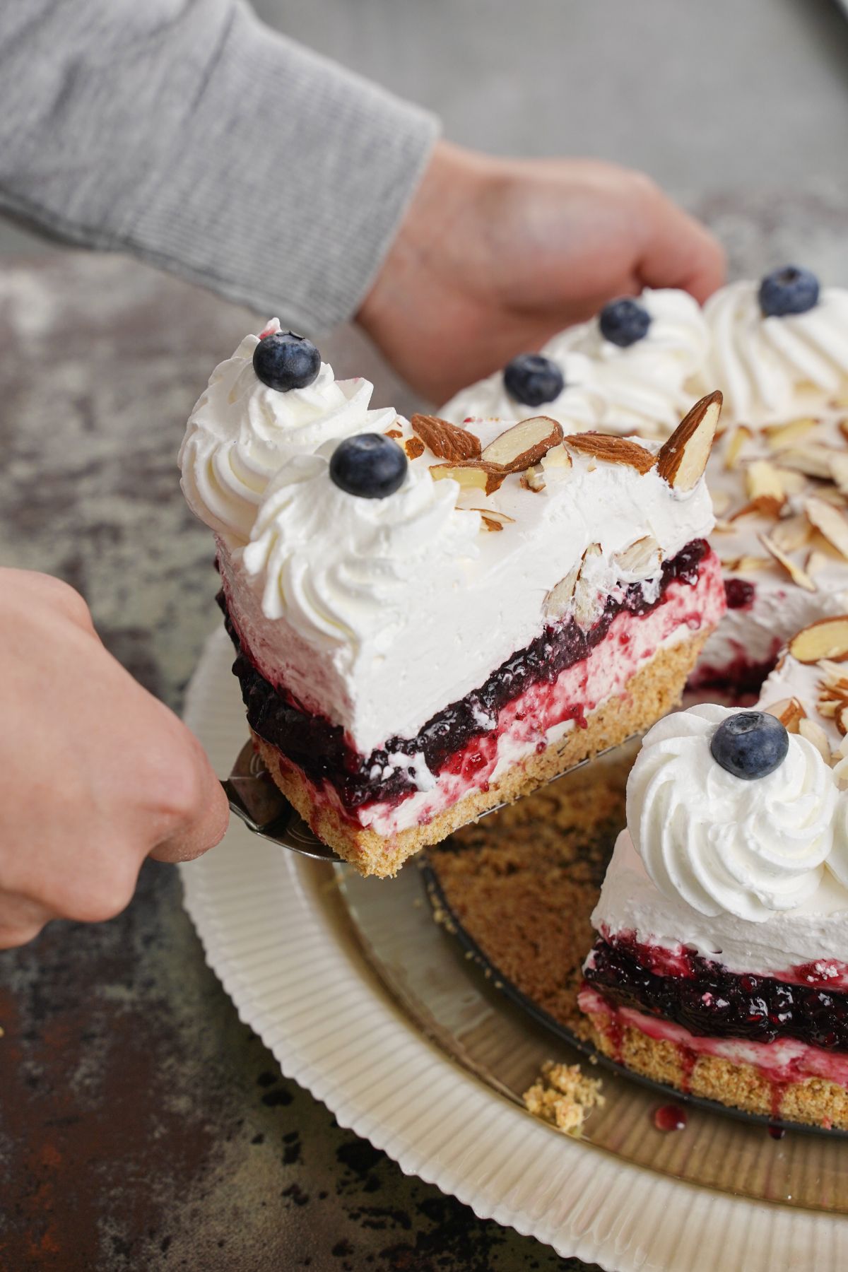 woman lifting blueberry cheesecake slice off cake platter