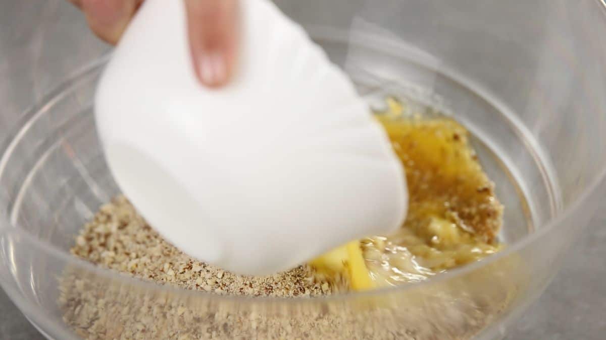 hand pouring butter into crushed cookies in glass bowl