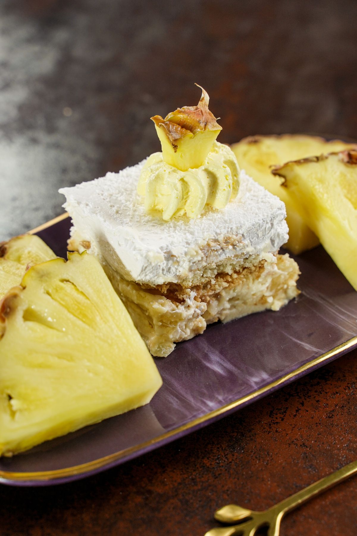 sliced Italian cream cake on purple platter with pineapple slices