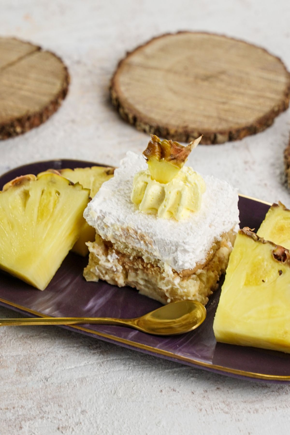 italian cream cake slice on platter with sliced pineapple on white table by wood slices