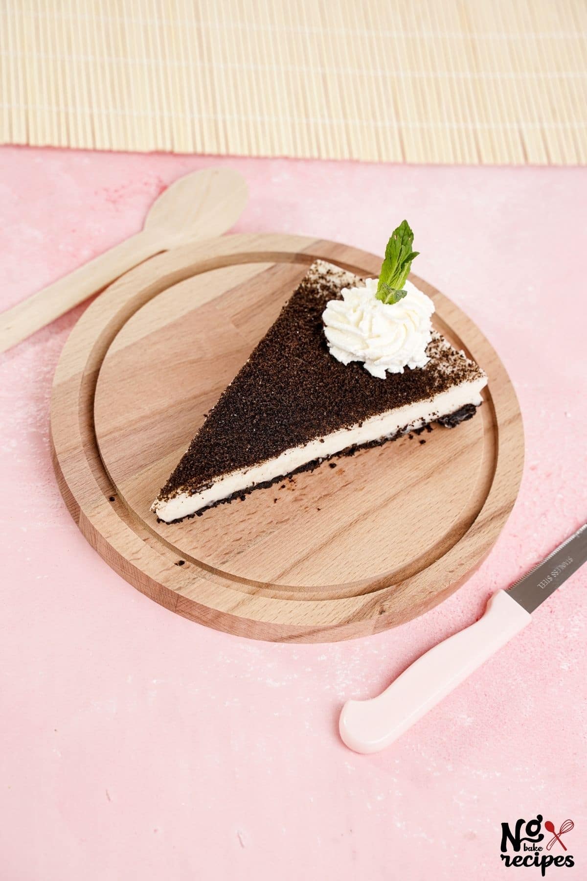 slice of cheesecake topped with whipped cream and mint sitting on wood plate on pink tablecloth