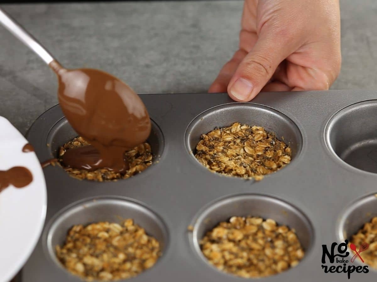 hand holding spoon of chocolate over oatmeal in muffin tin
