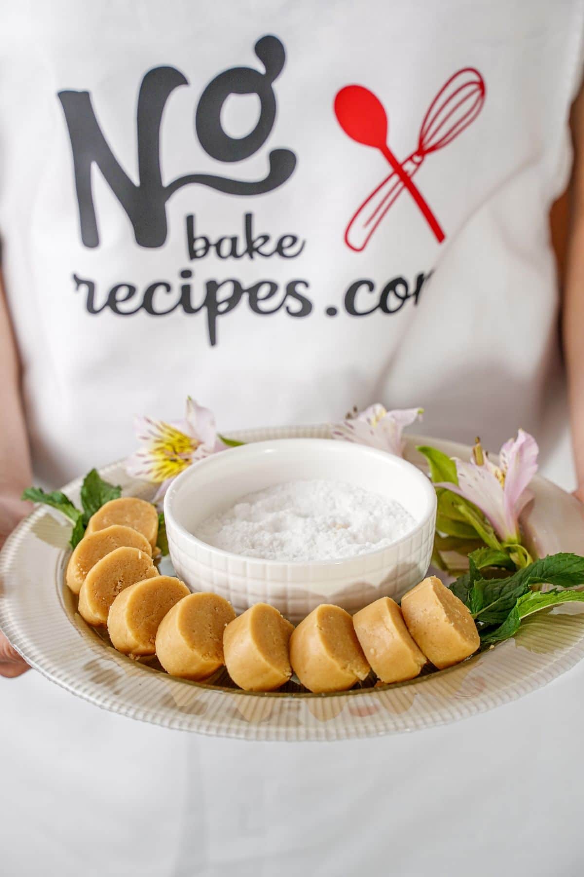 woman in no bake recipe apron holding platter of peanut butter candy
