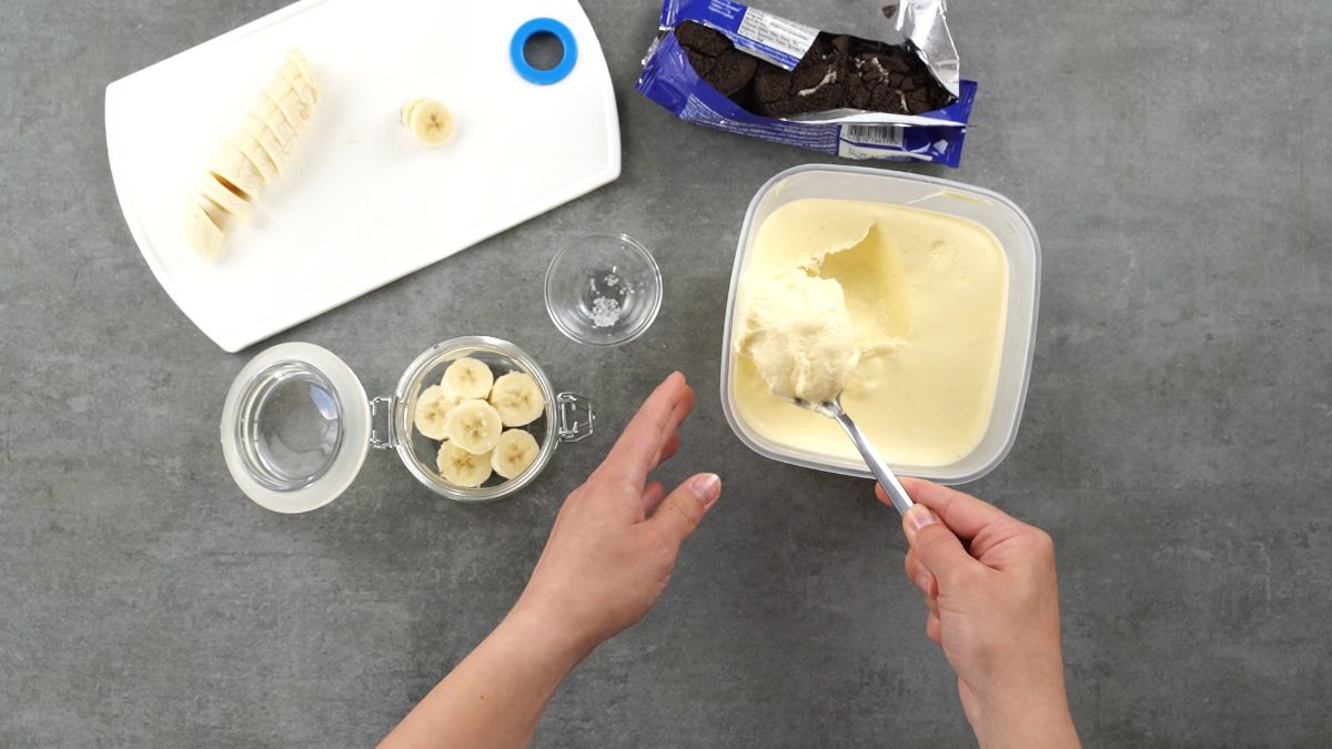 hand scooping ice cream from tub into dessert glass on gray table
