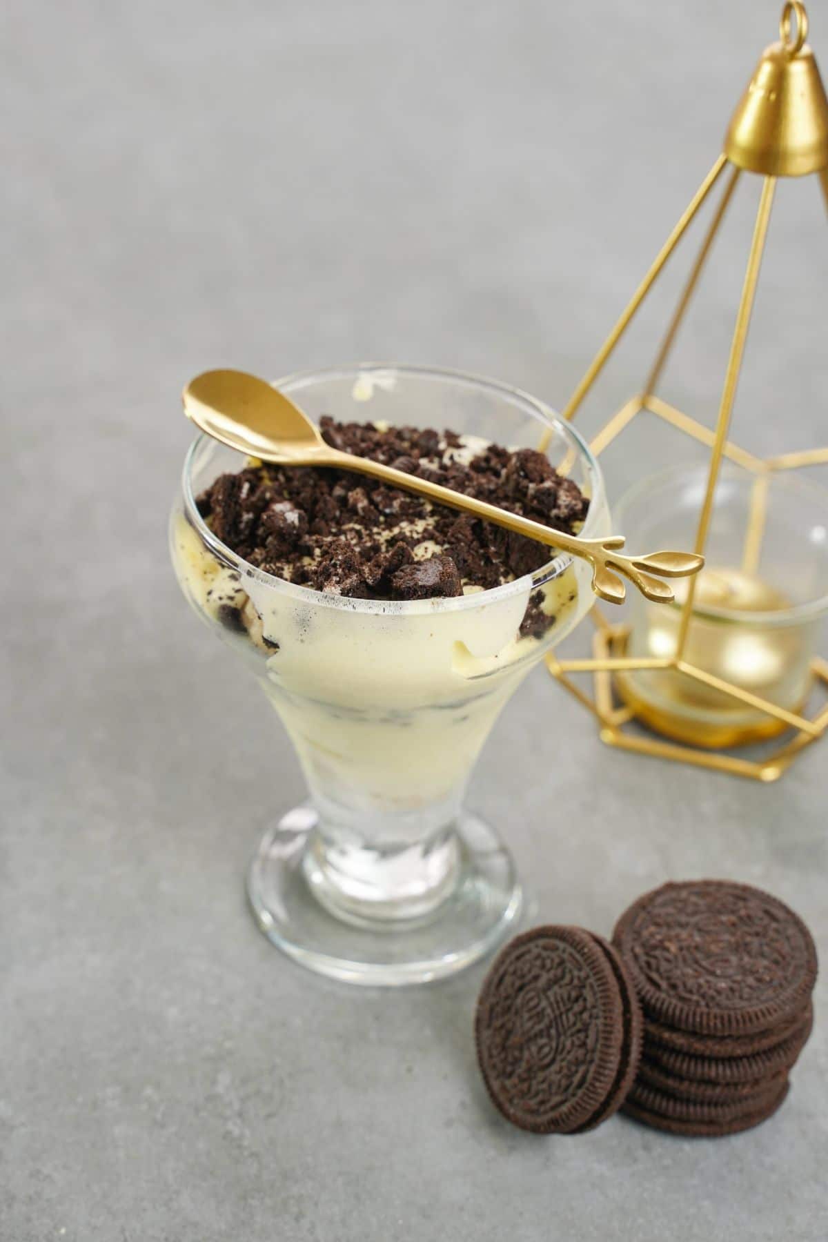 glass dessert cup of parfait with oreo cookies on gray table with gold spoon on top