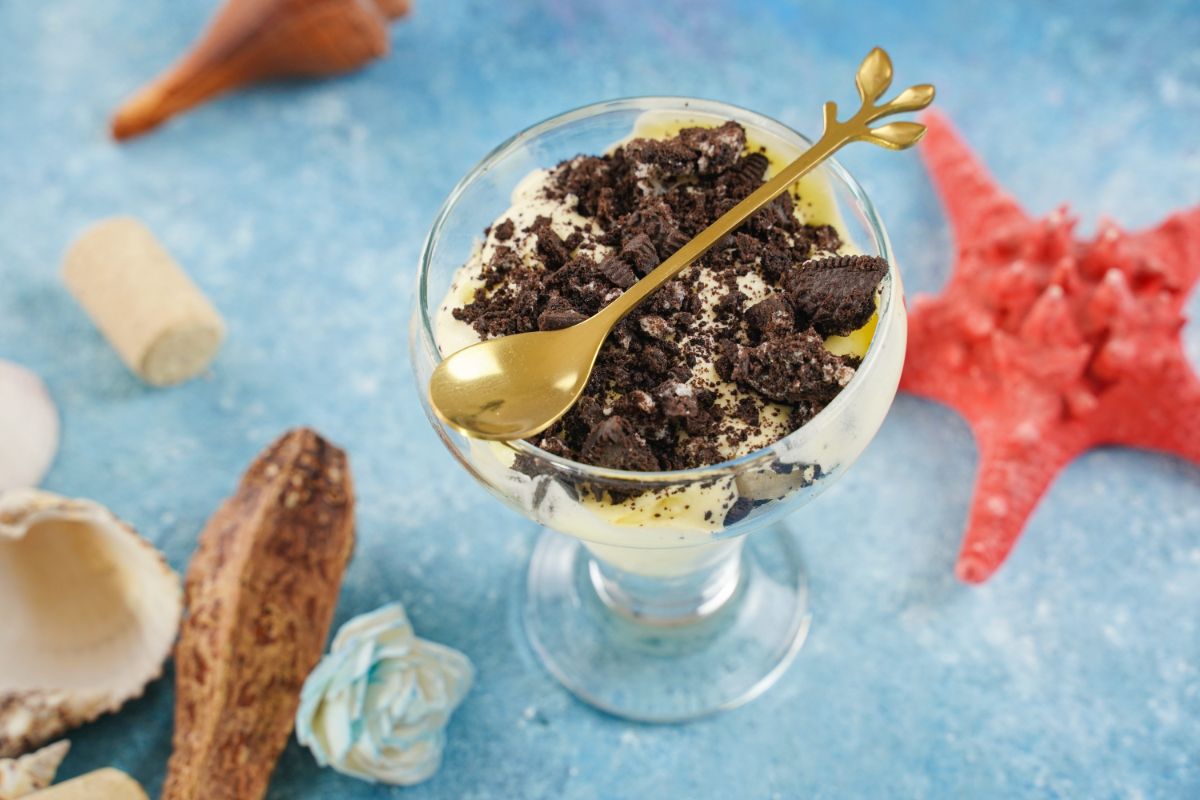 dessert cup of oreo pudding with gold spoon on top sitting on blue table by fake starfish