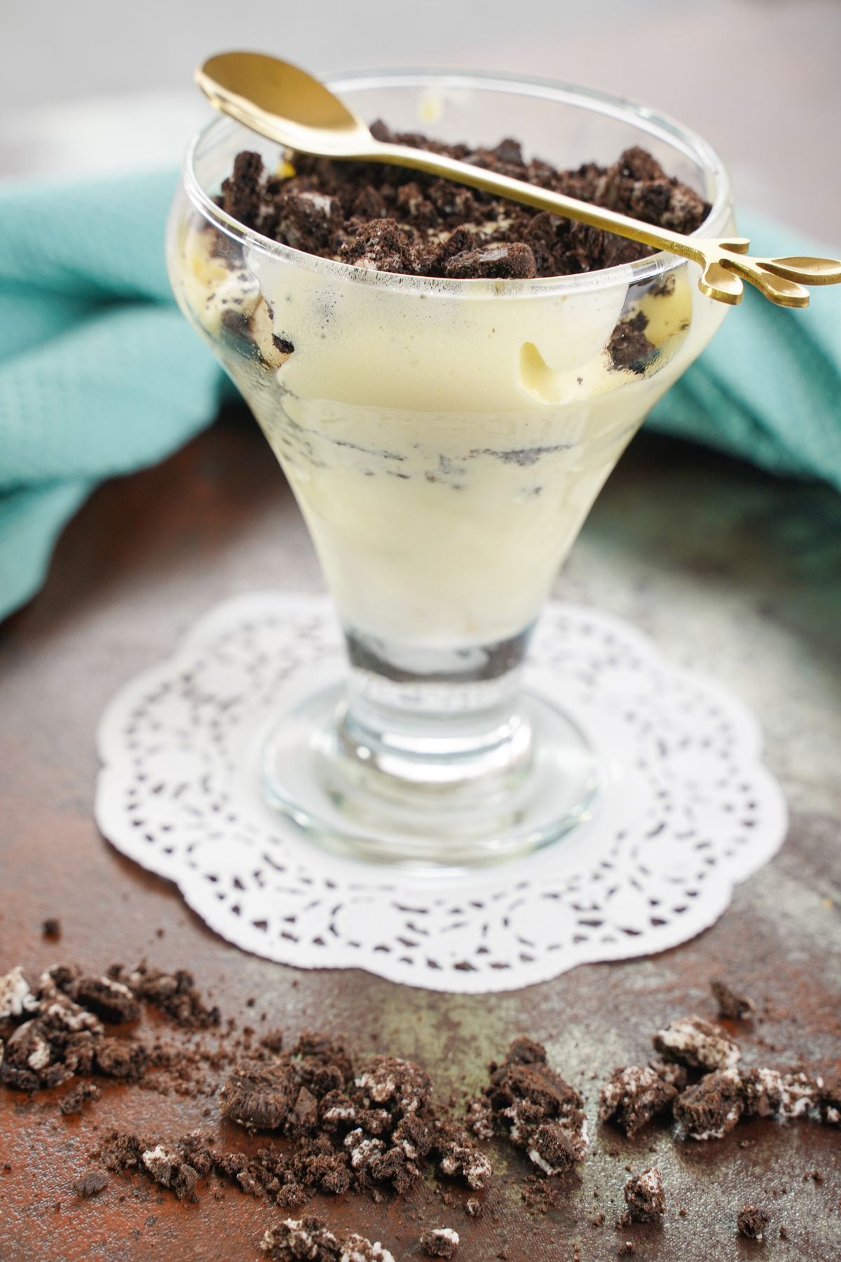 glass dessert cup of pudding and oreos on white doily on table by blue napkin