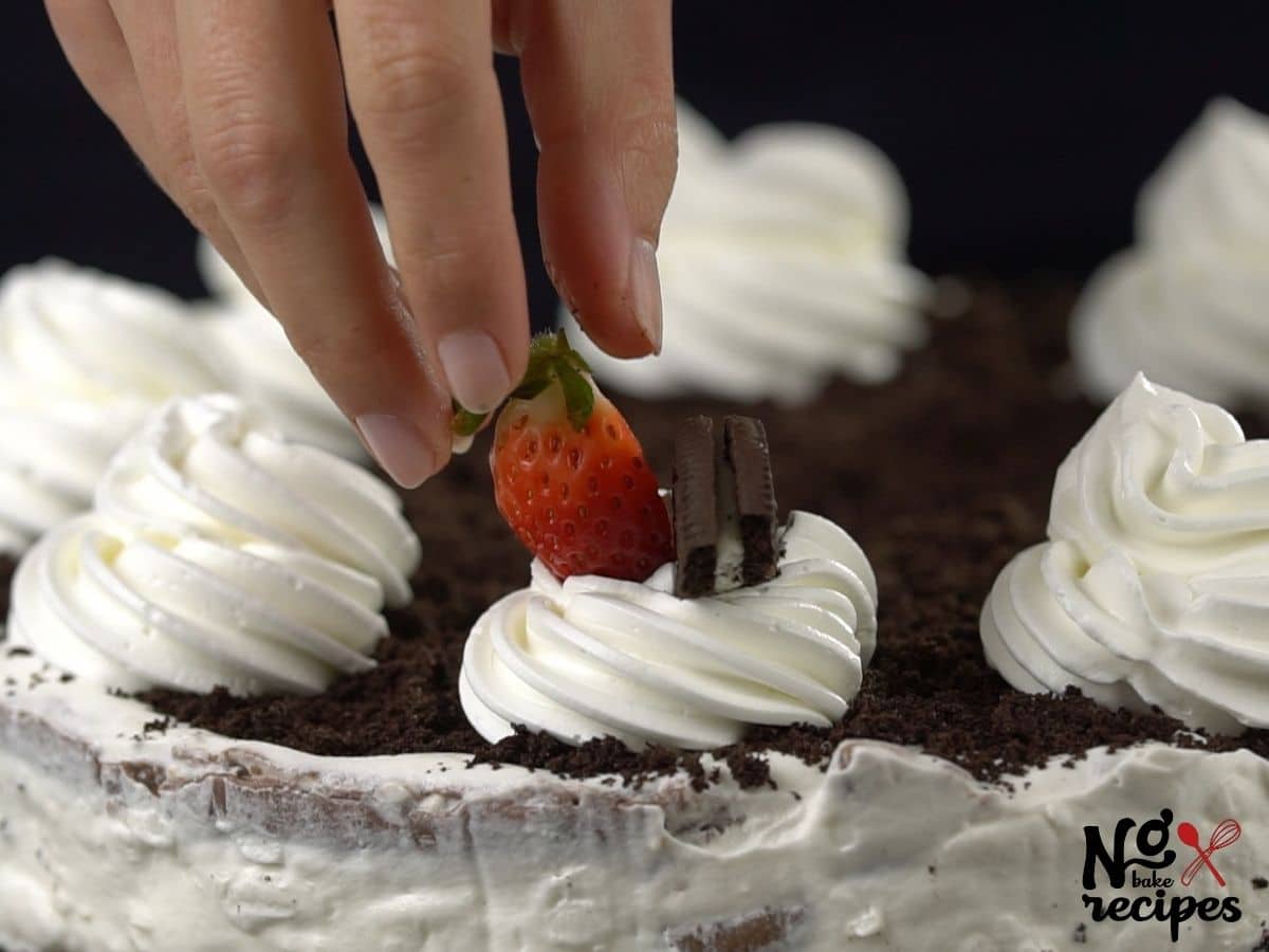 hand placing berry on top of whipped cream on cake
