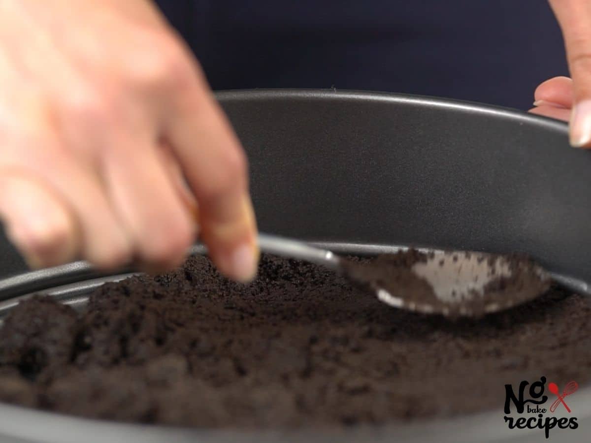 hand using spoon to press cookies into springform pan