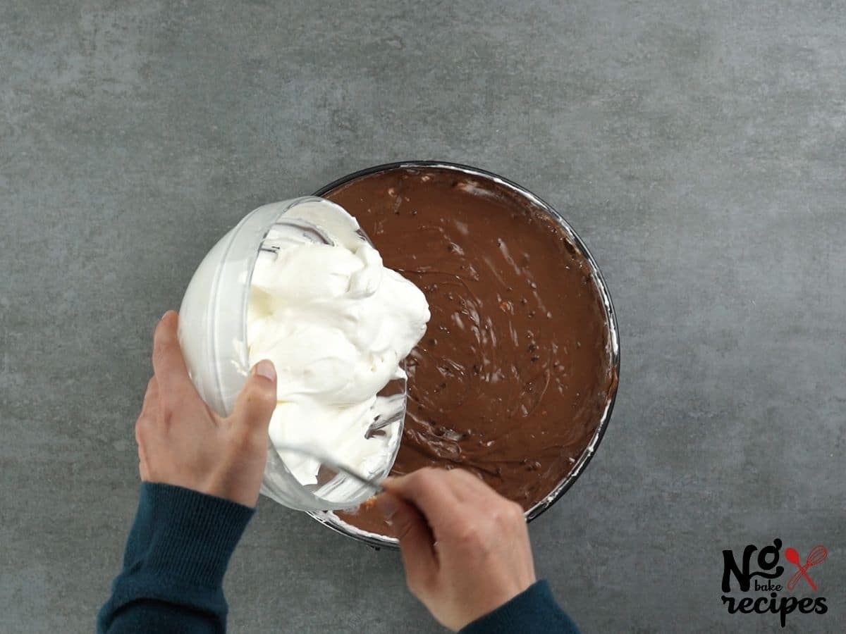 hand pouring whipped cream over pudding in pie plate