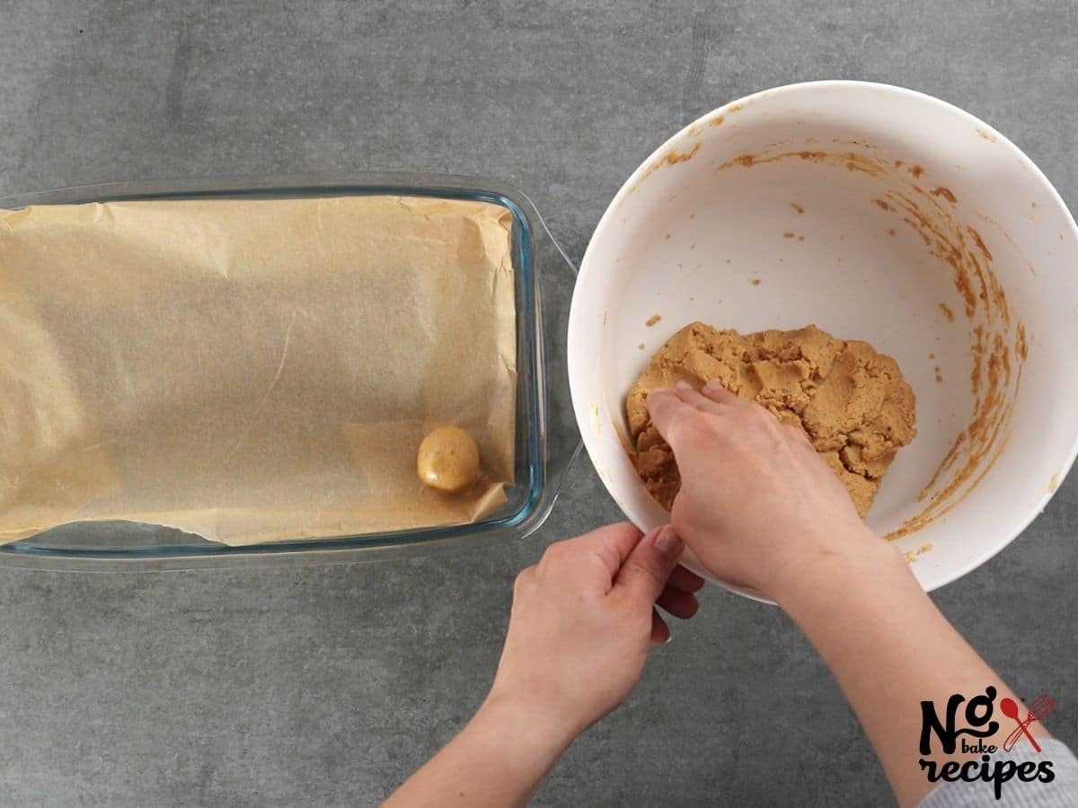 hand rolling peanut butter balls in white bowl onto parchment paper