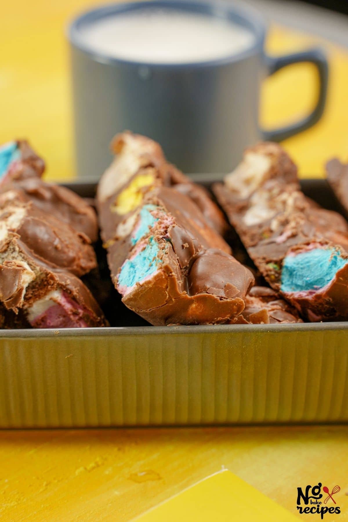 container of rocky road bars on yellow table by mug of milk