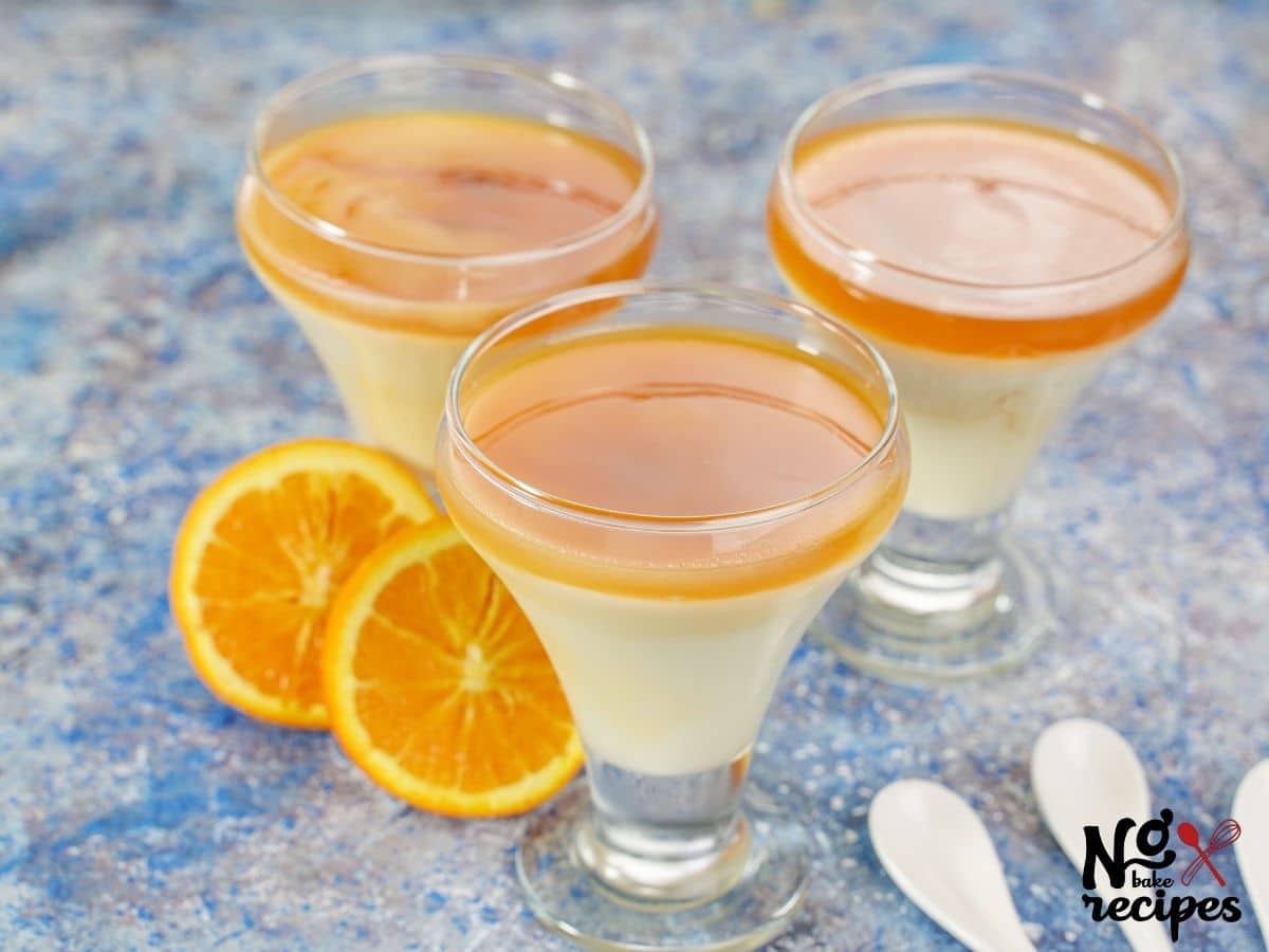 three dessert glasses of pudding on blue table by orange slices