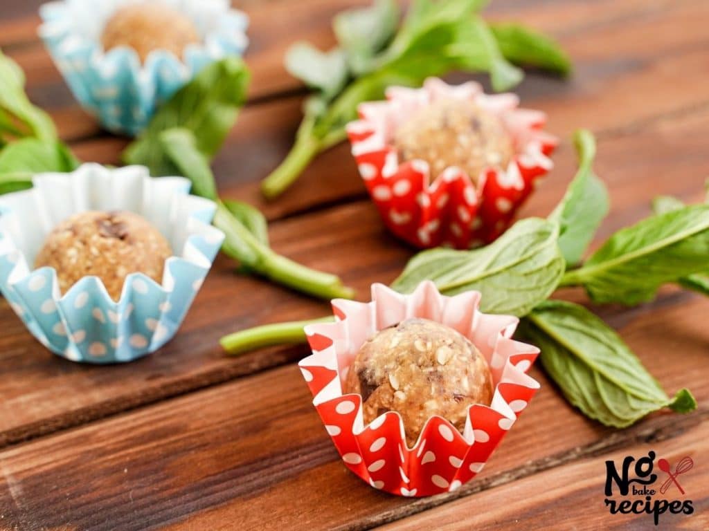 four protein balls in wrappers on wood table by flowers