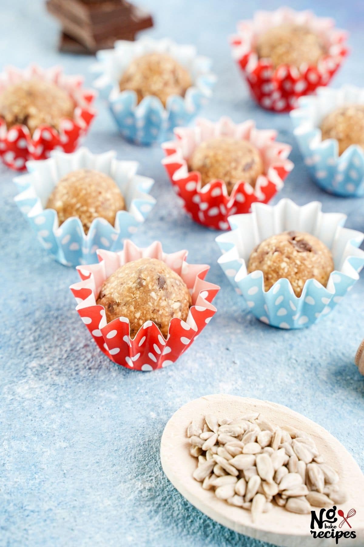 vegan protein balls in wrappers on blue table by sunflower seeds