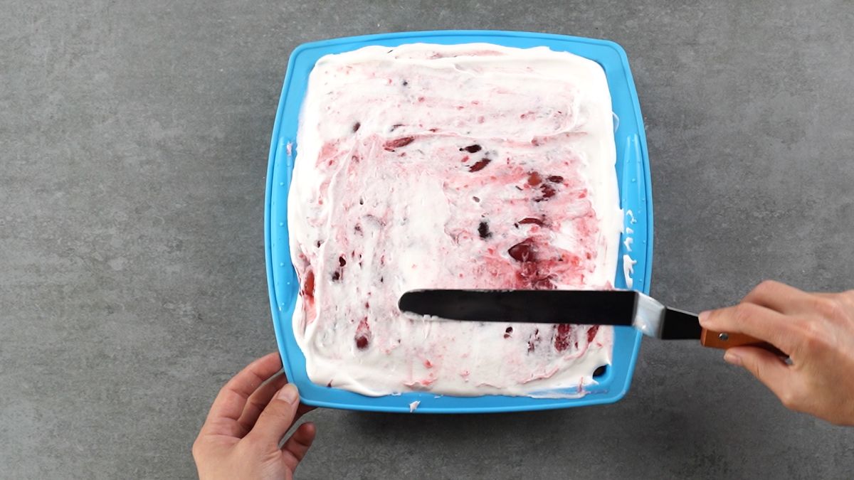 hand spreading whipped topping over top of cake