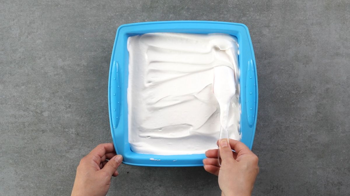 hand spreading cool whip over top of cake in blue pan