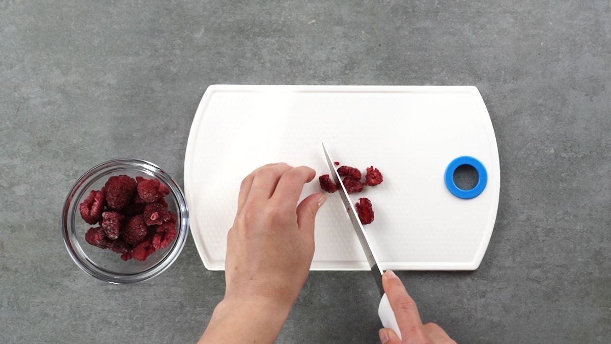 hand cutting berries into pieces on white cutting board
