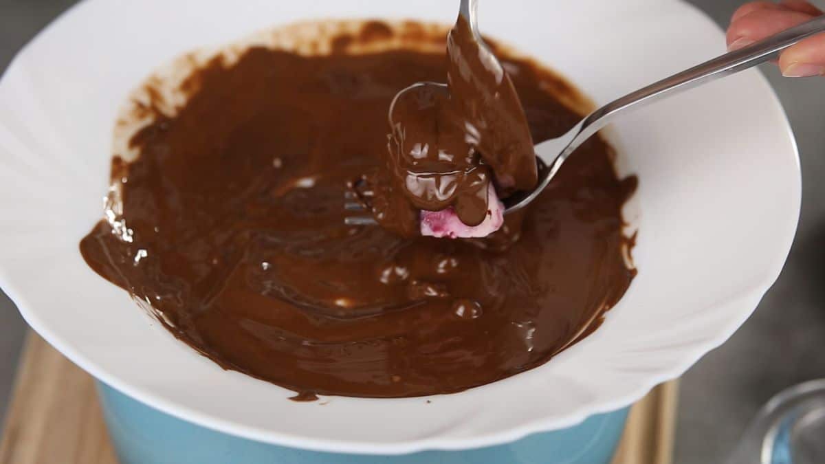 bonbon being dipped into bowl of chocolate