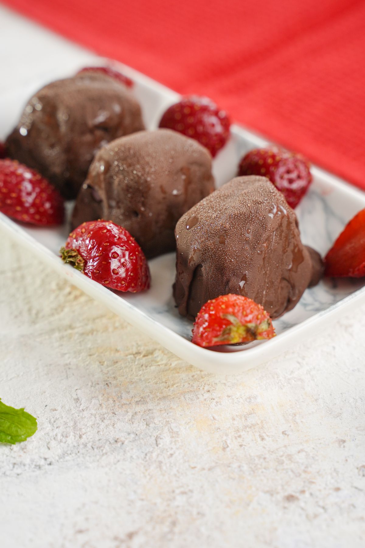 white bowl of chocolate bonbons with strawberries sitting on white table with red napkin