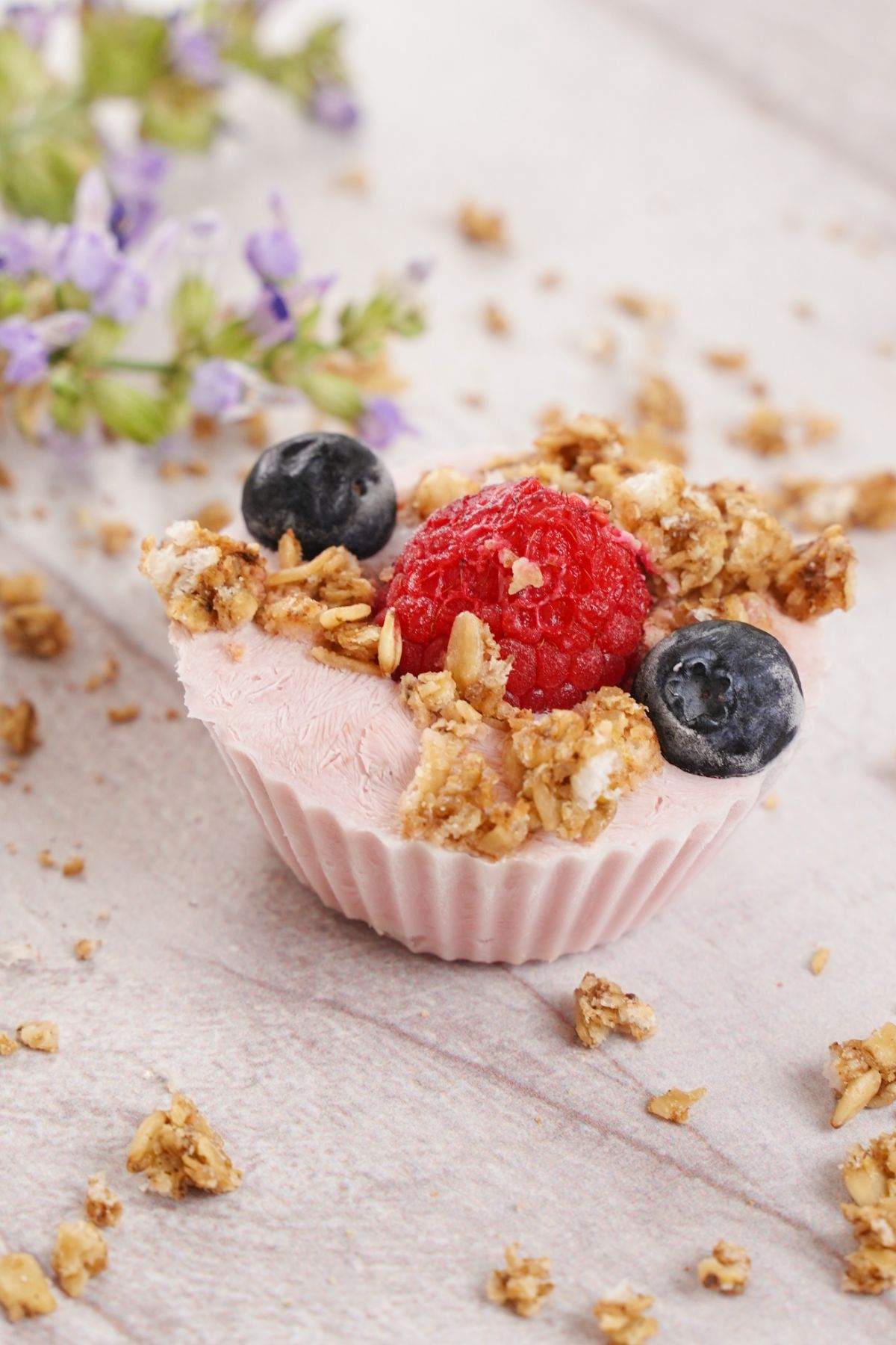 yogurt cup with berries on top sitting on table with granola bits
