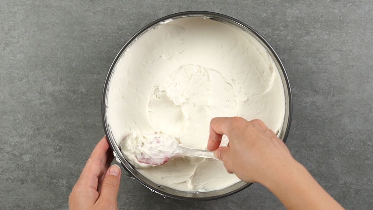 hand spreading cream cheese onto crust