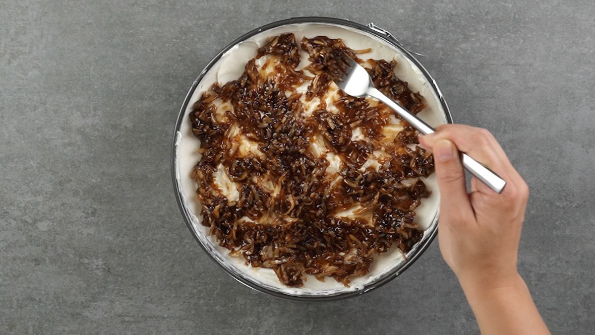 fork spreading caramel and coconut over top of pie