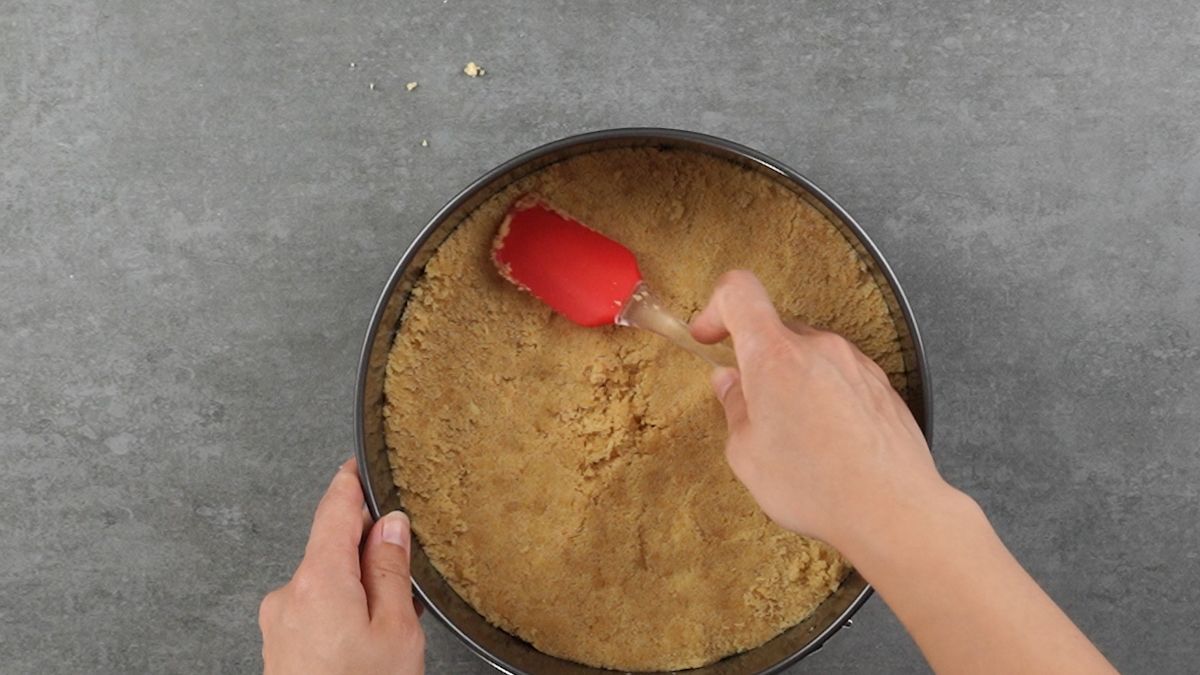 red spatula pressing cookie crumbs into springform pan