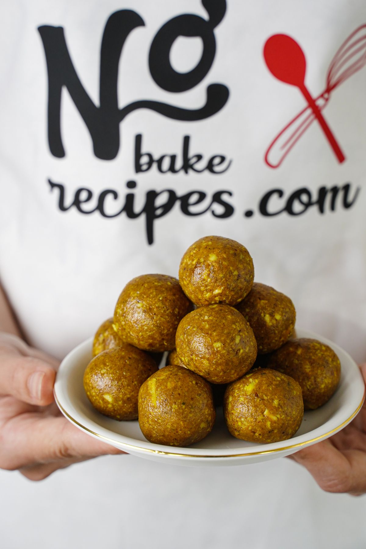 lady in no bake recipes apron holding white plate stacked with golden milk energy balls