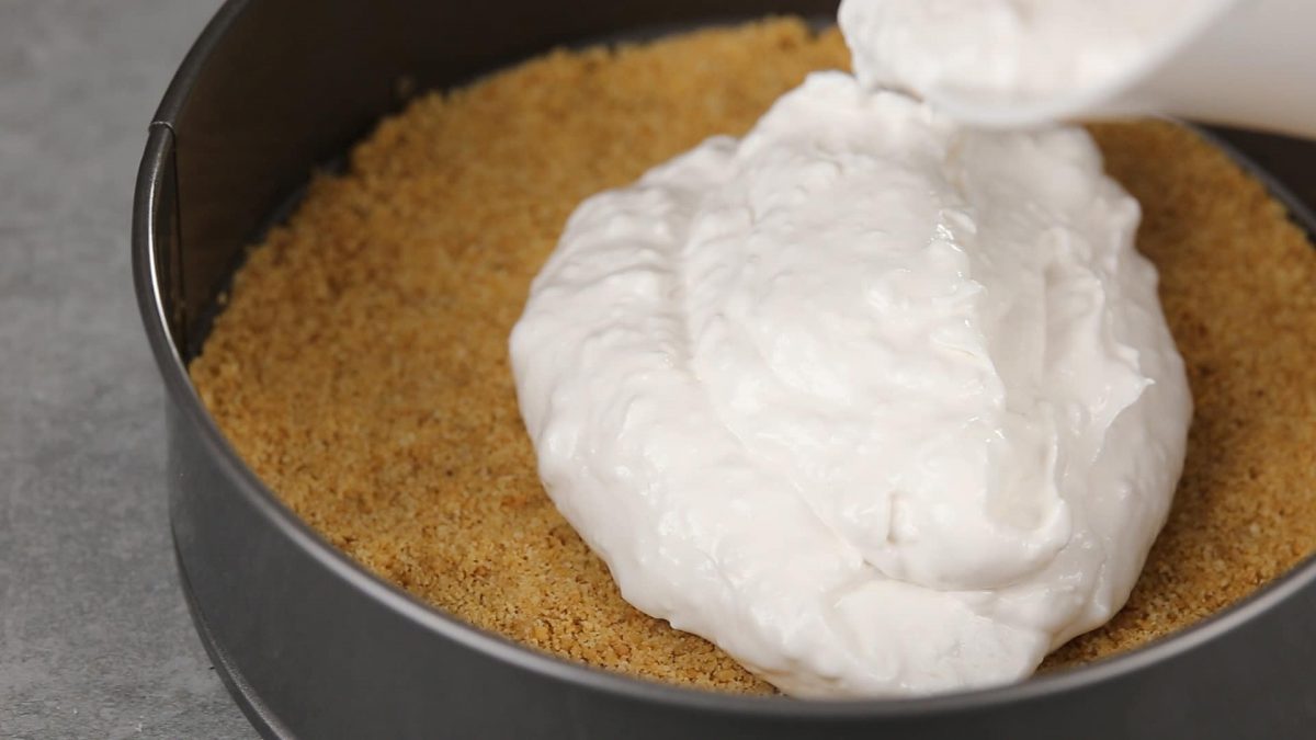 pouring cheesecake over top of graham cracker crust