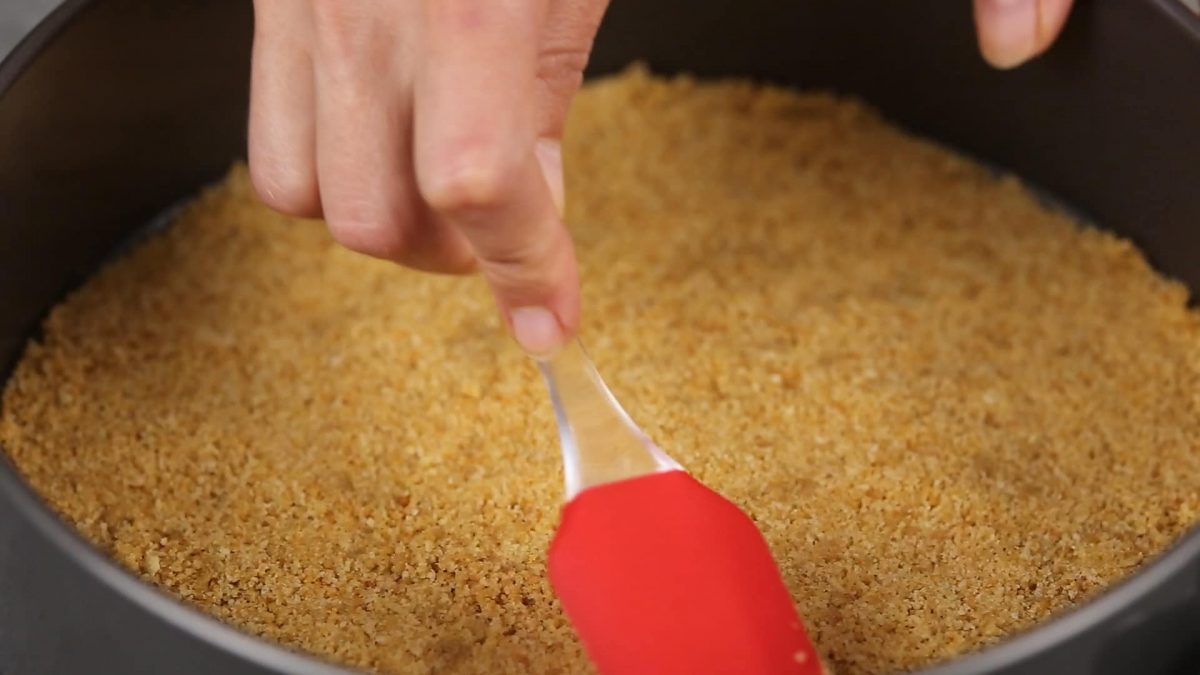 red spatula pressing cookie crumbs into springform pan