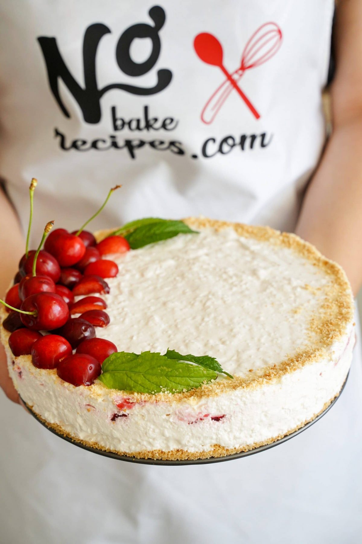 lady holding cheesecake topped with fresh cherries on side