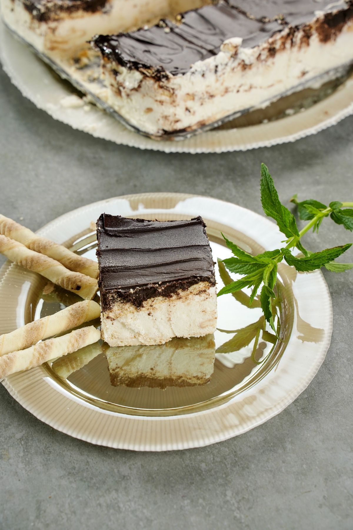 gray table with a gold plate holding a slice of cake in front of larger platter of no bake eclair cake