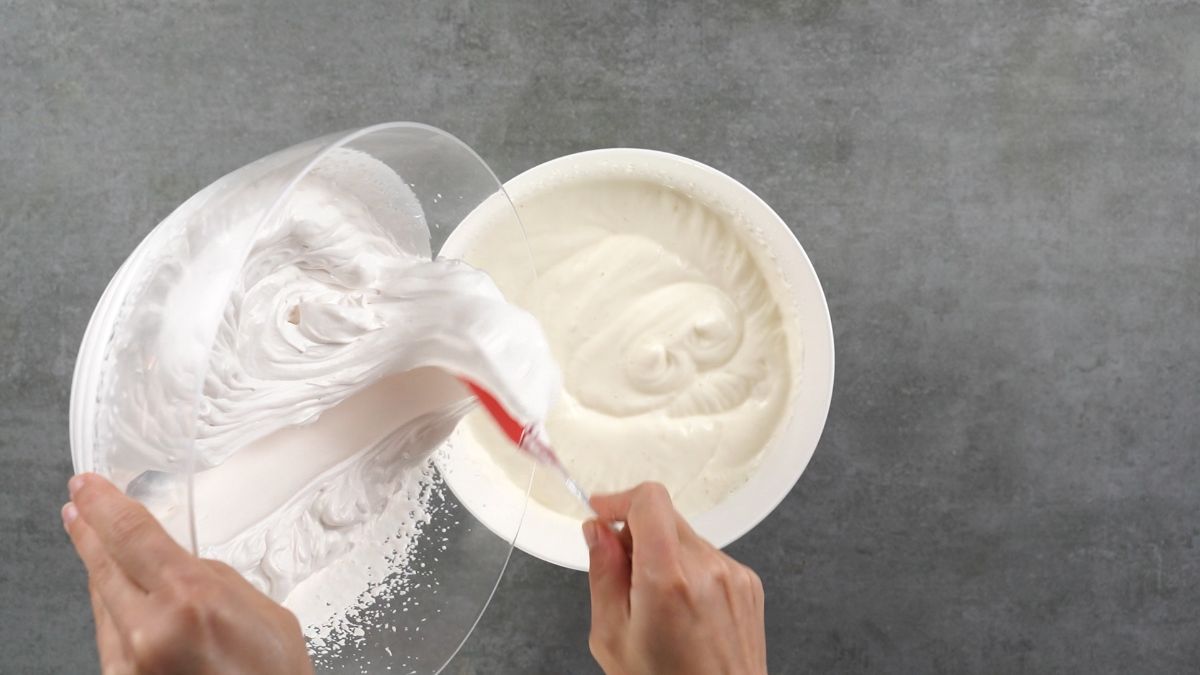hand pouring whipped cream out of glass bowl into white bowl of pudding