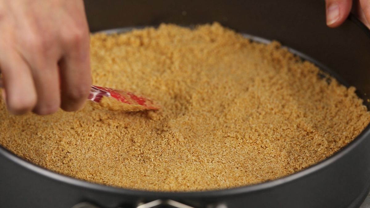 red spatula spreading cookie crumbs into springform pan