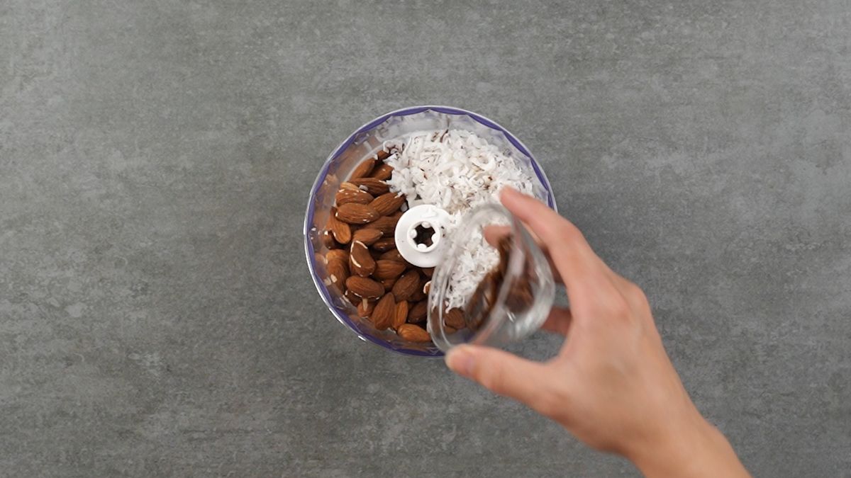 Crushing almonds, coconut, and Medjool dates in a food processor