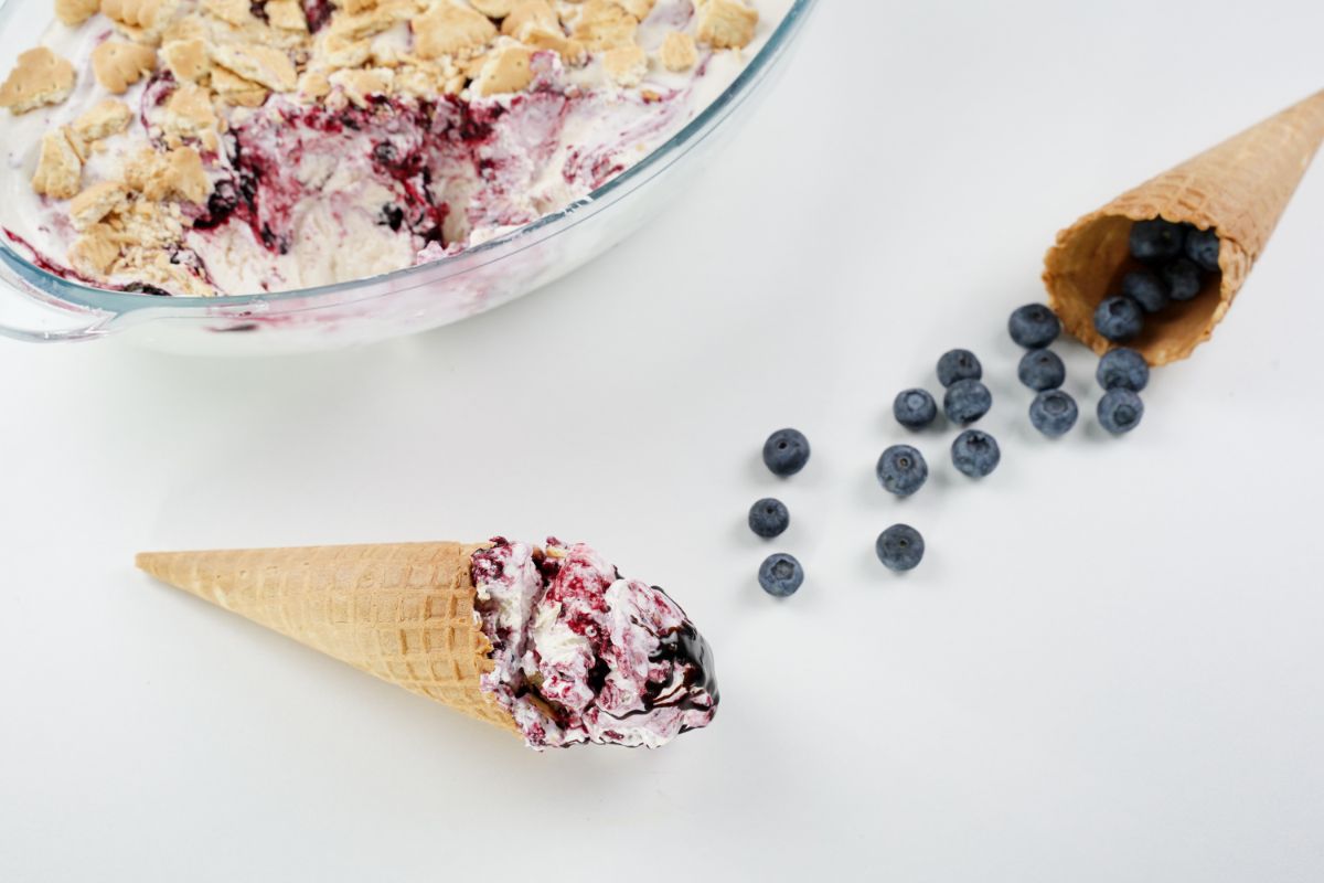 No Churn Blueberry Cheesecake Ice Cream in cone with some fresh blueberries