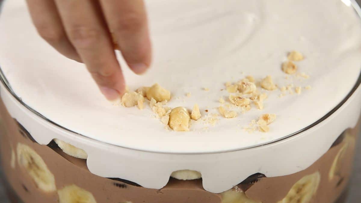 hand sprinkling hazlenuts on top of whipped cream on bowl