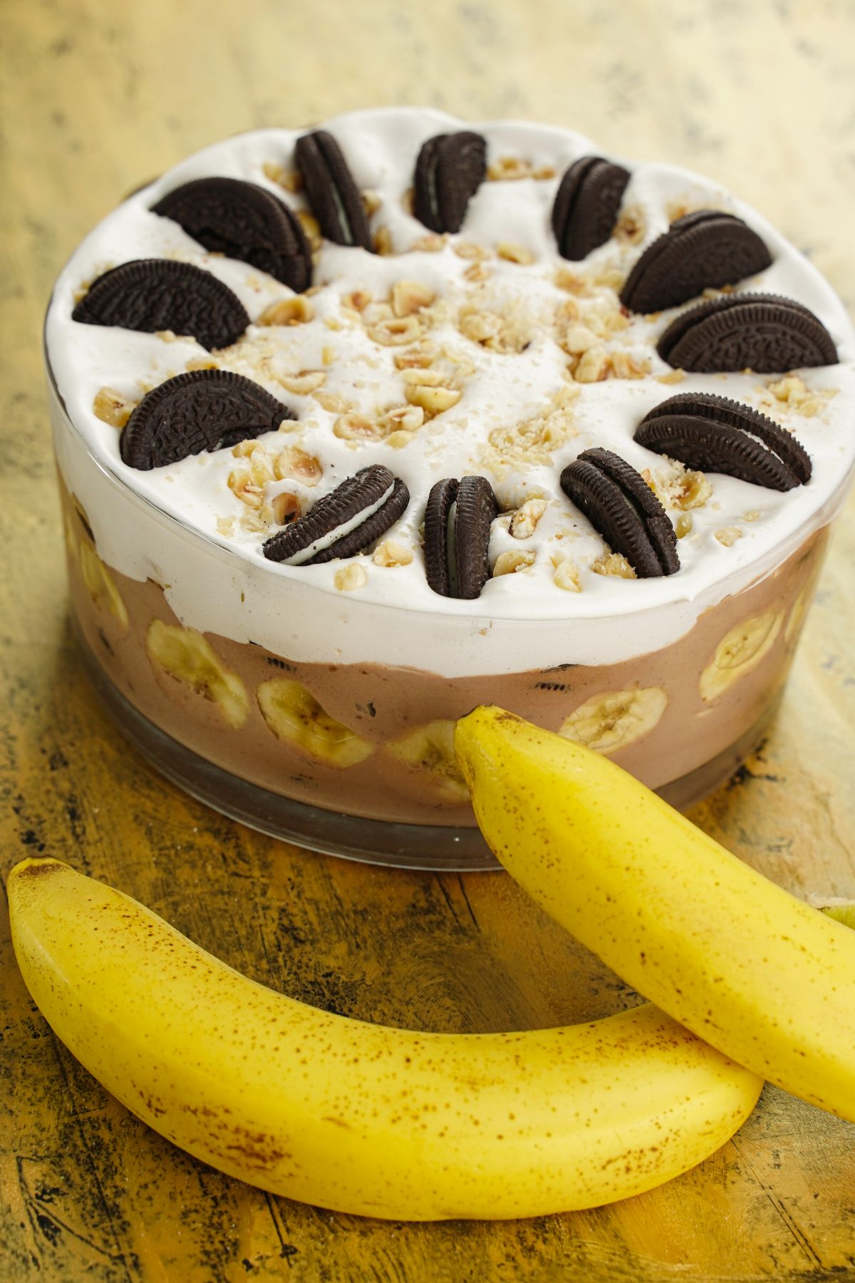 trifle bowl topped with whipped cream and Oreo cookis on wood table by bananas