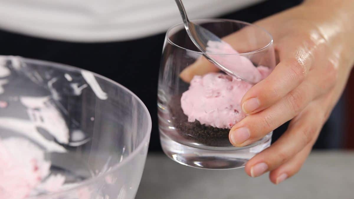 spoon putting pink pudding in glass with cookie crumbs