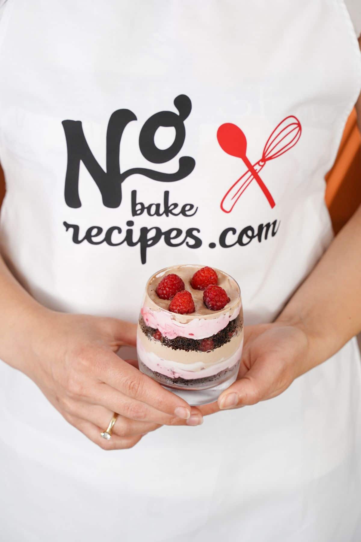 Woman in no bake recipes apron holding parfait in glass topped with raspberries