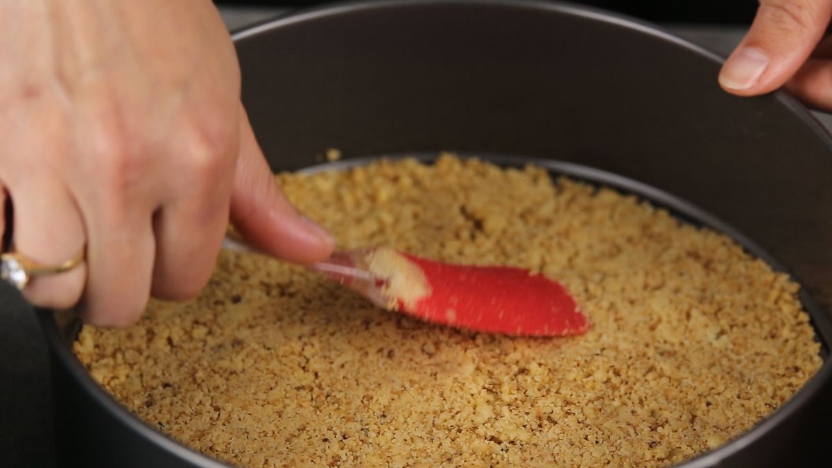 red spatula pressing crumbs into springform pan