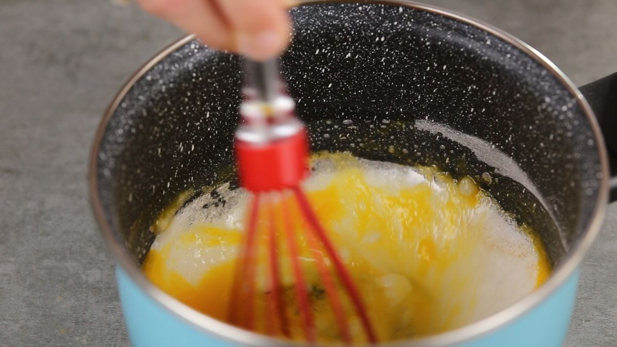 red whisk mixing egg into flour in blue pan