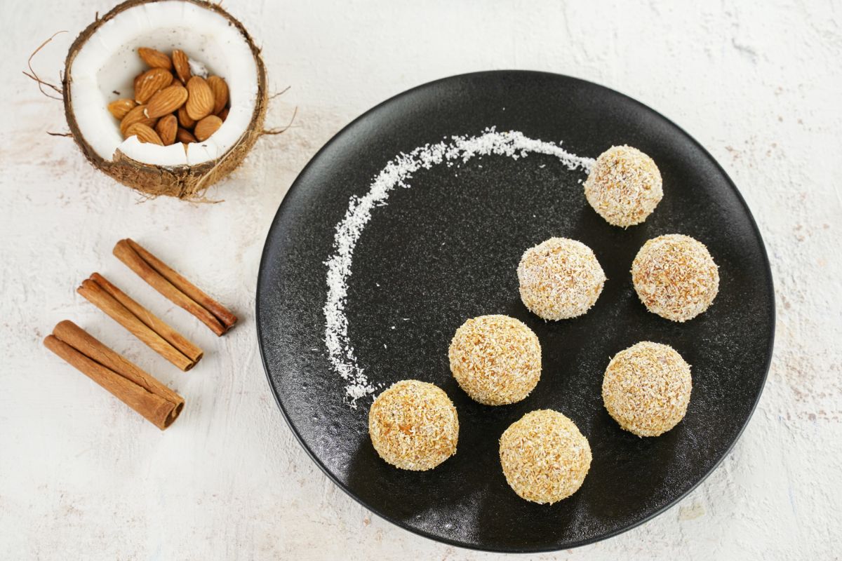 No-Bake Carrot Balls served in a plate with cinnamon stick and half coconut filed with almonds in the background