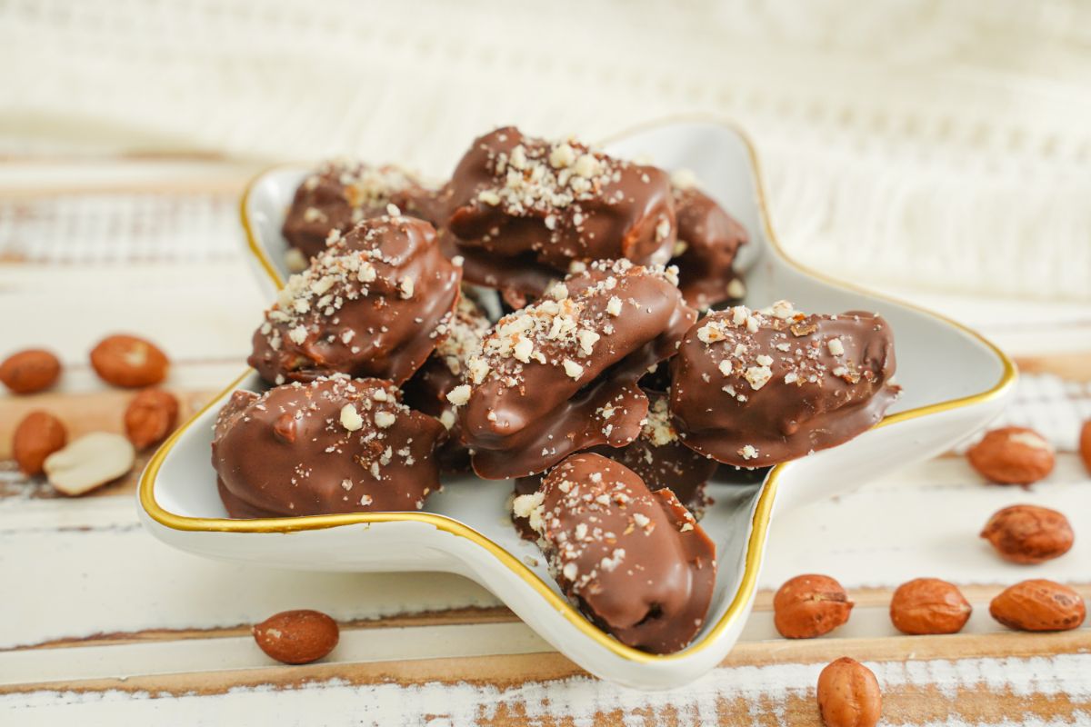 Chocolate Covered Peanut Stuffed Dates served on a plater with some fresh peanuts in the background 