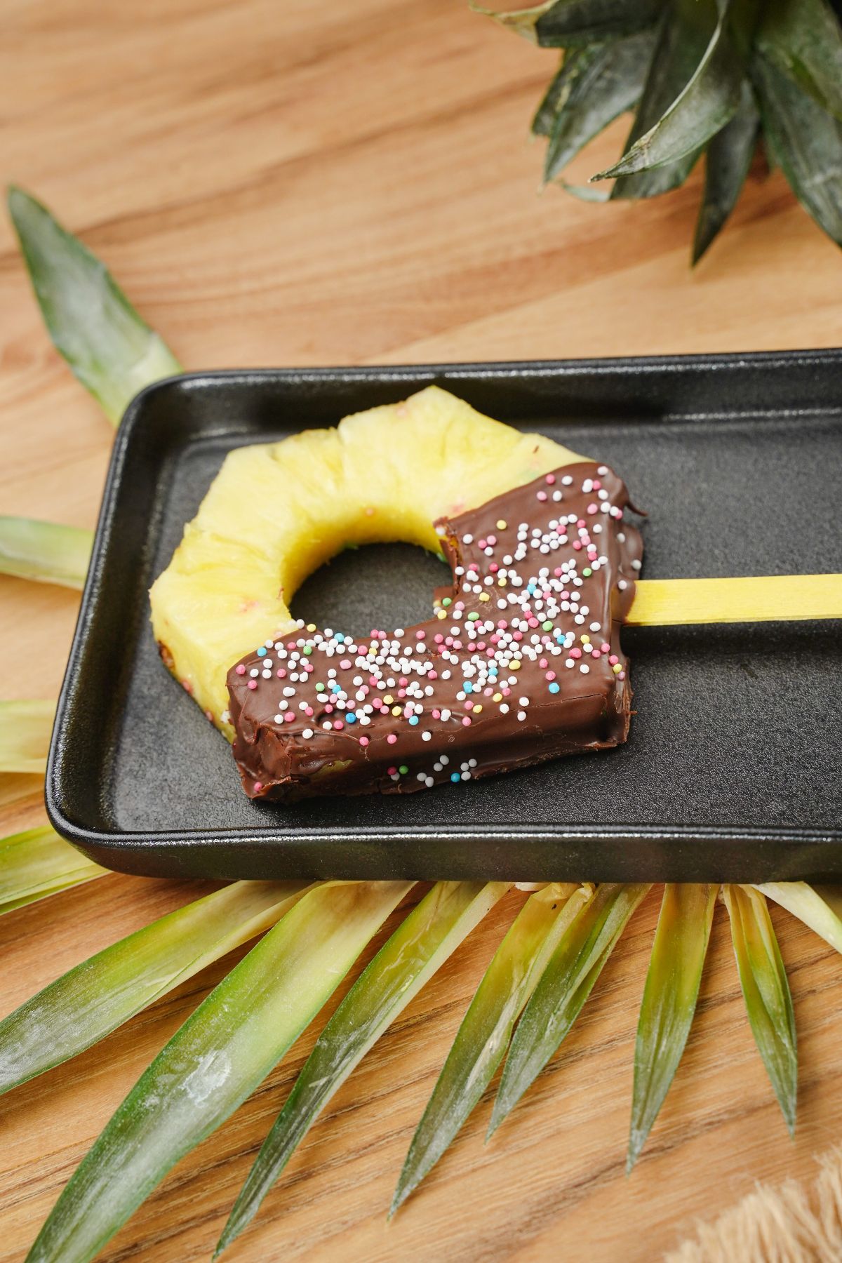vertical view of Chocolate Coated Pineapple Pop on a black tray
